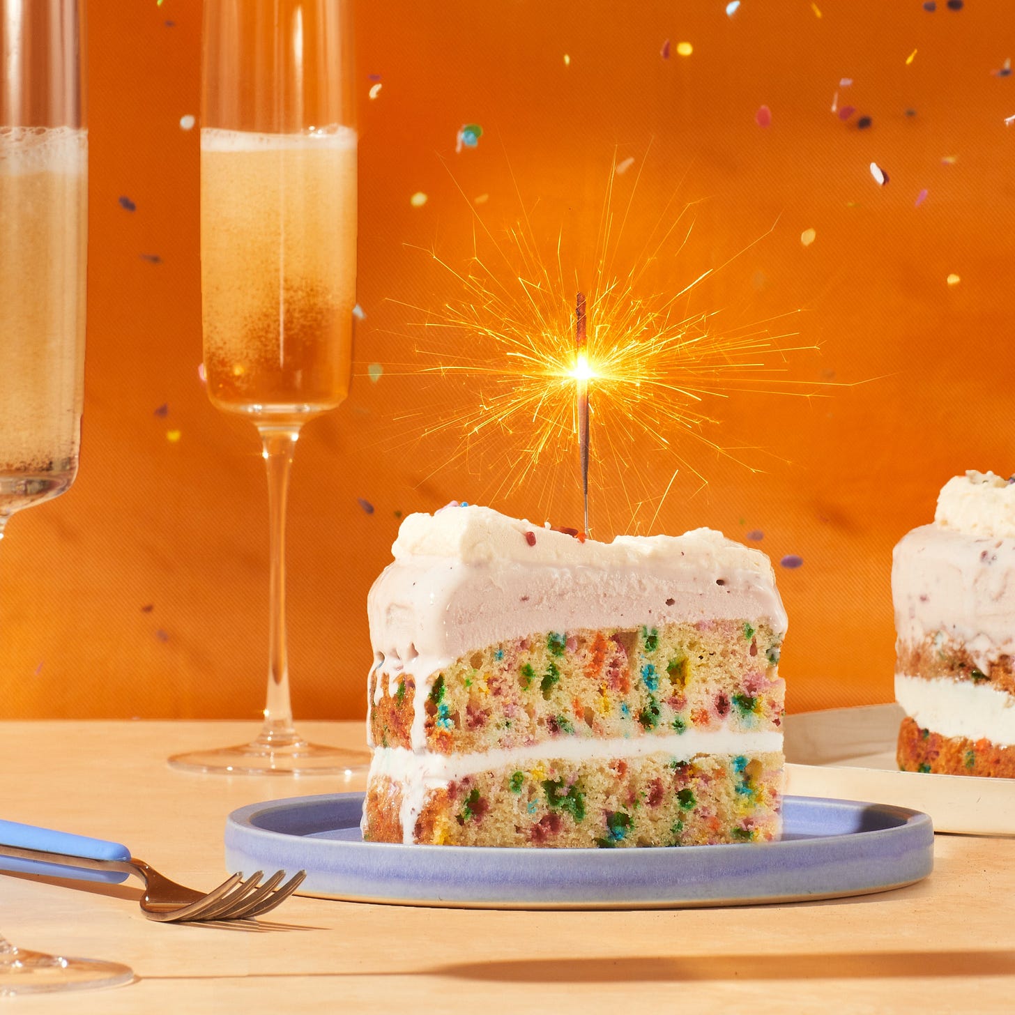 Ice Cream Birthday Cake with a candle lit on top and champagne flutes to the side