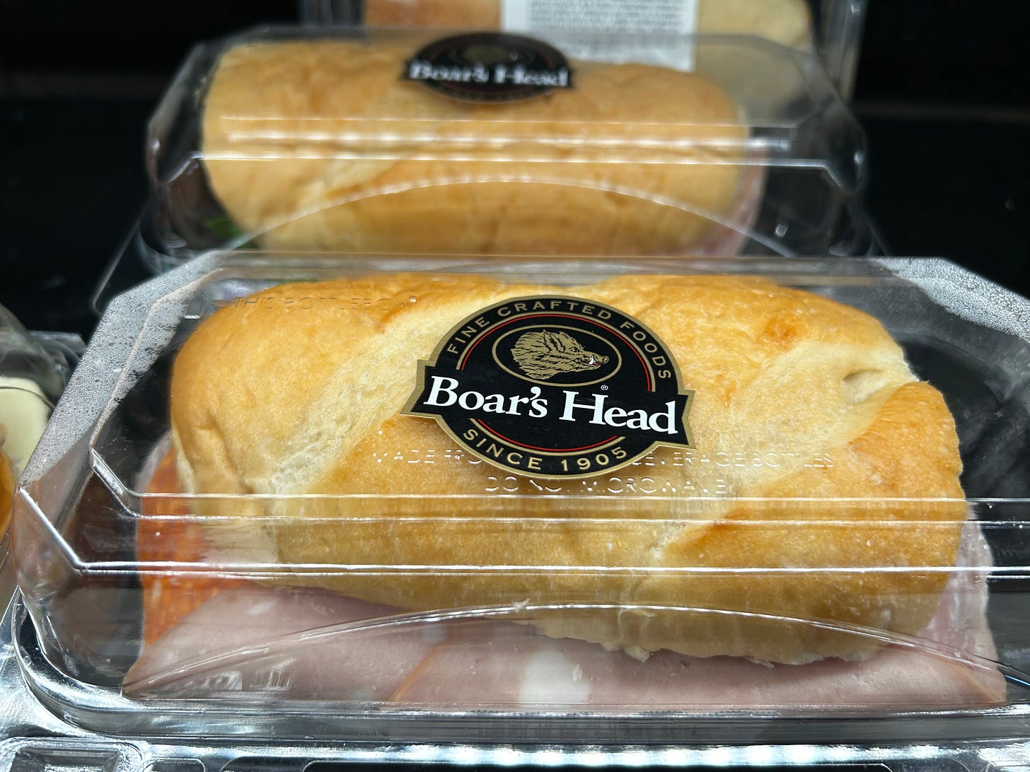 Boar's Head meat sandwich in a plastic box in the supermarket refrigerator case.