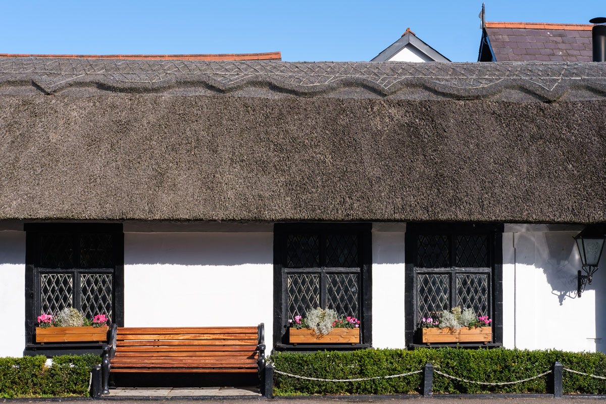 A brown thatched roof on a white building, with windows in view and a bench in front of the building A brown thatched roof on a white building, with windows in view and a bench in front of the building