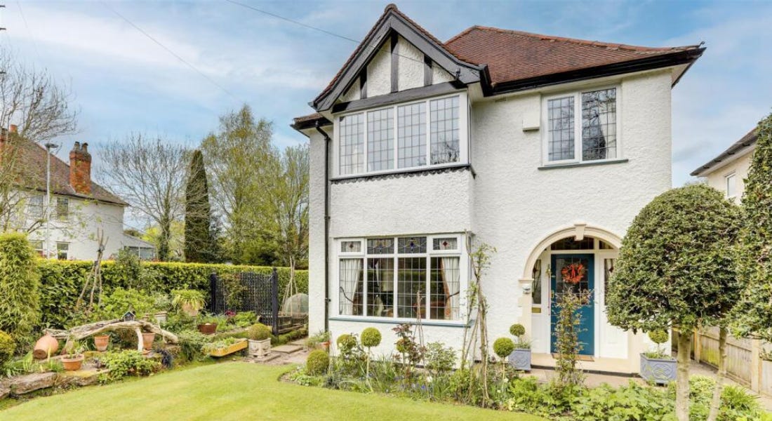 A white house with a blue door with a lawn and hedges around it and a blue sky above it