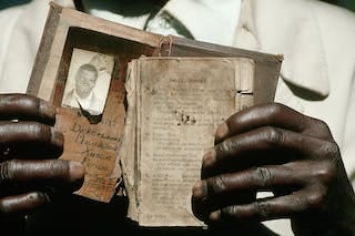 Close up of hands holding an old, battered document containing an identity photo and personal information. Close up of hands holding an old, battered document containing an identity photo and personal information.