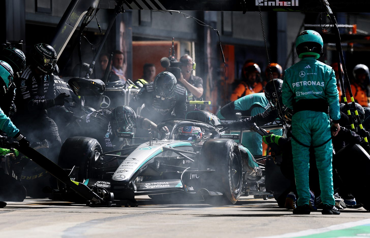 Mercedes mechanics work on Kimi Antonelli's car in the pit box as smoke pours out from the brakes