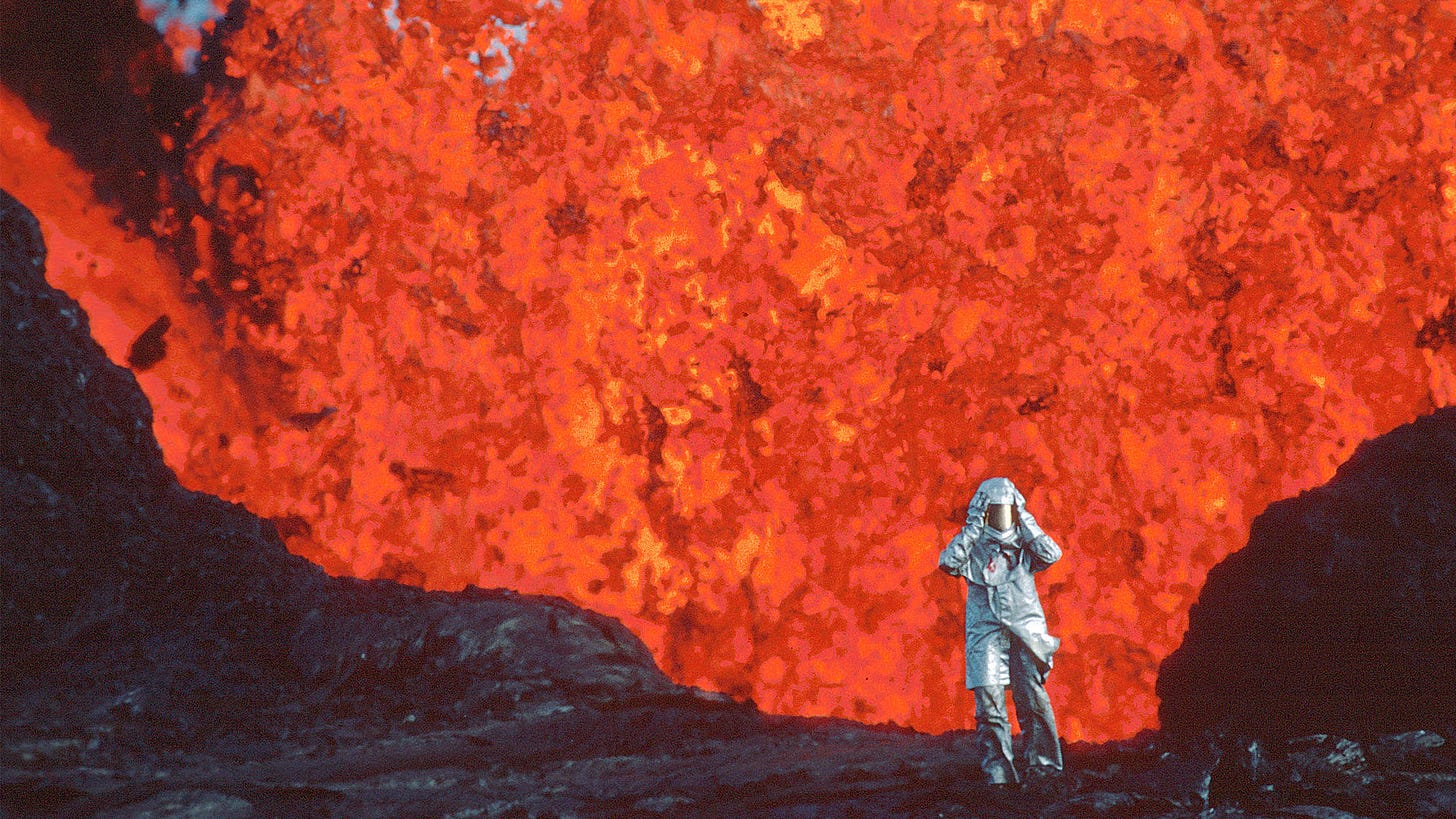 A figure in a silver mylar outfit next to a wall of lava in a still from Fire of Love