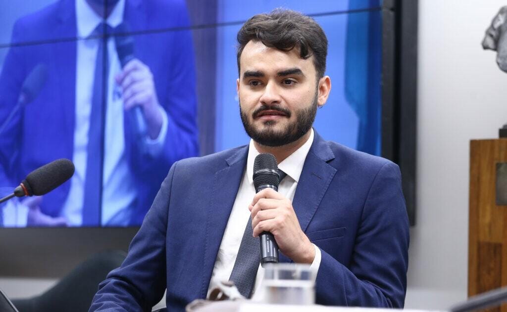 Homem de terno e gravata com microfone na mão O conteúdo gerado por IA pode estar incorreto. Homem de terno e gravata com microfone na mão O conteúdo gerado por IA pode estar incorreto.