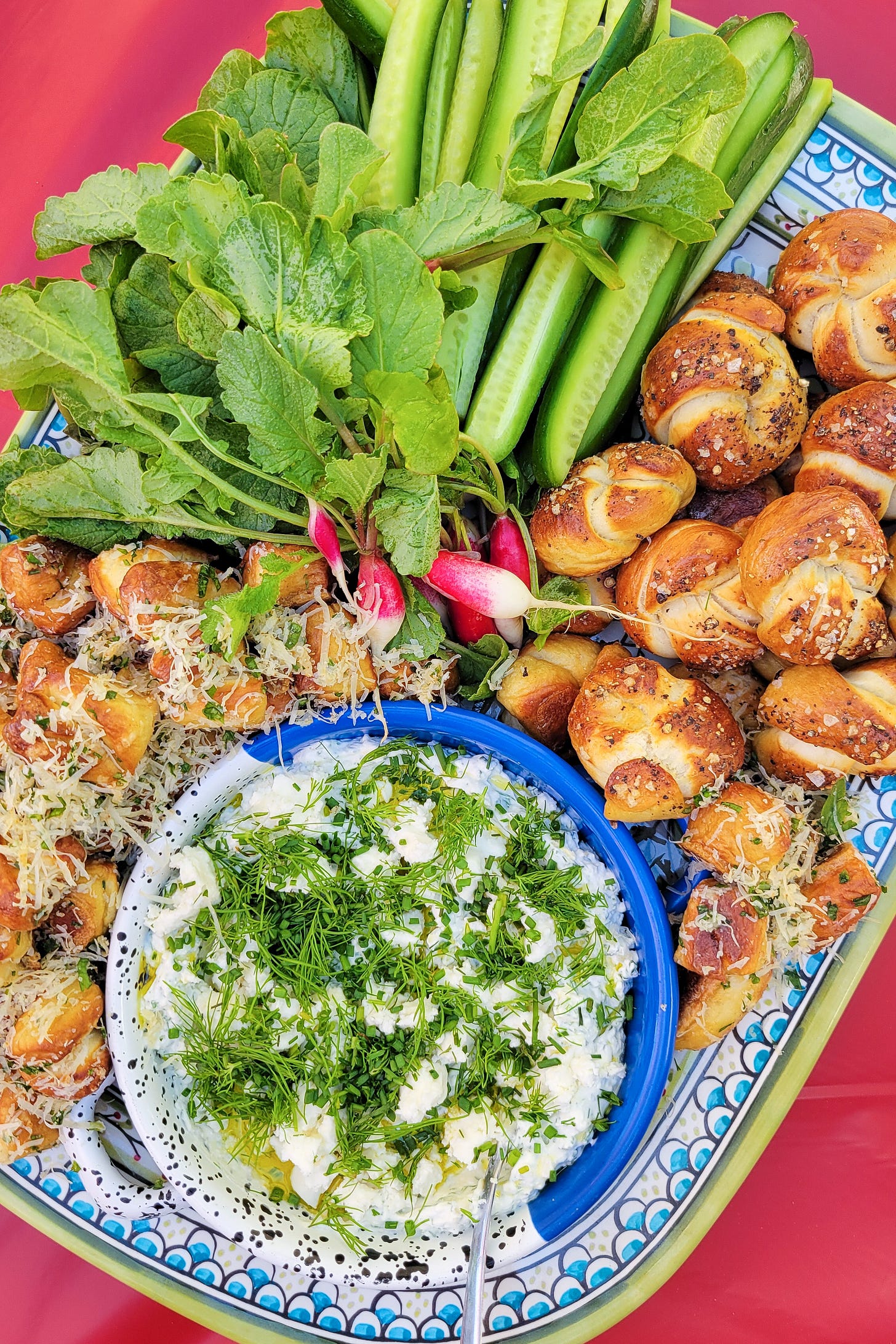 Platter with a bowl of feta-labneh dip, soft pretzels, radishes, and cucumbers