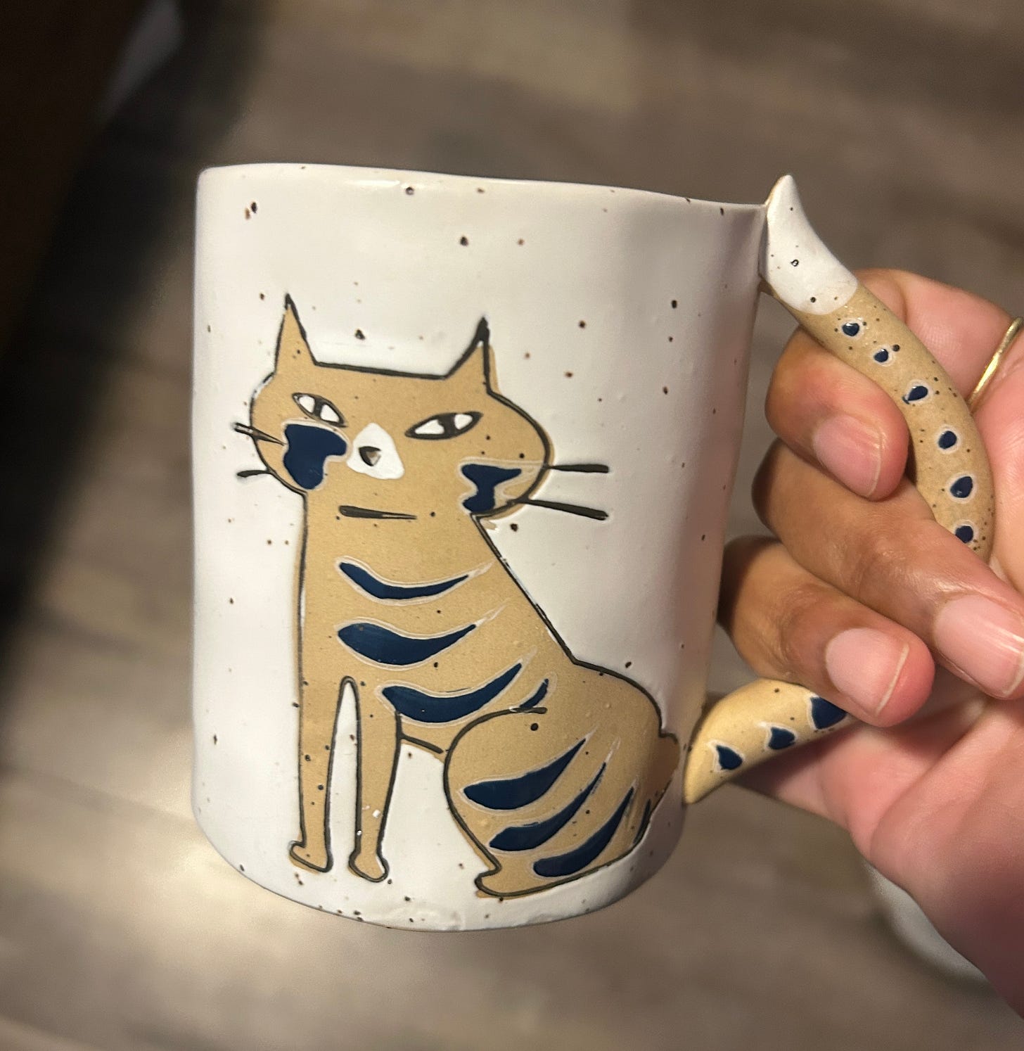 a photo of Nisha's cat mug while she holds the handle in the shape of a cat's tail