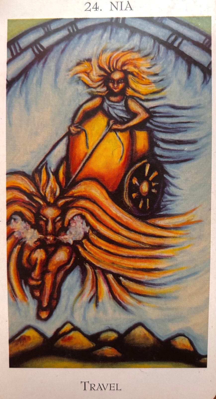 Close-up of an Enochian Tarot card that says 24. NIA Travel. The background is a pale blue sky with a domed roof at the top. The central subject is a woman with wild blonde hair. She stands on a golden chariot holding the reigns of a golden pegasus with steam coming out of its nostrils. She looks as if she’s flying towards you. There are distant brown mountains. The 24. is where the card itself sits in the overall order. It’s the 24th card in the stack. NIA is the Enochian name of the region. This is one of the major arcana cards that embodies more of an idea than the title of the being on the card, which is typical of the lesser arcana cards.