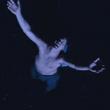 a shirtless man with his arms outstretched is kneeling in the rain