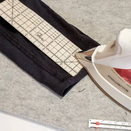 measuring and ironing the folds for a double folded hem on pants with a hot hem ruler