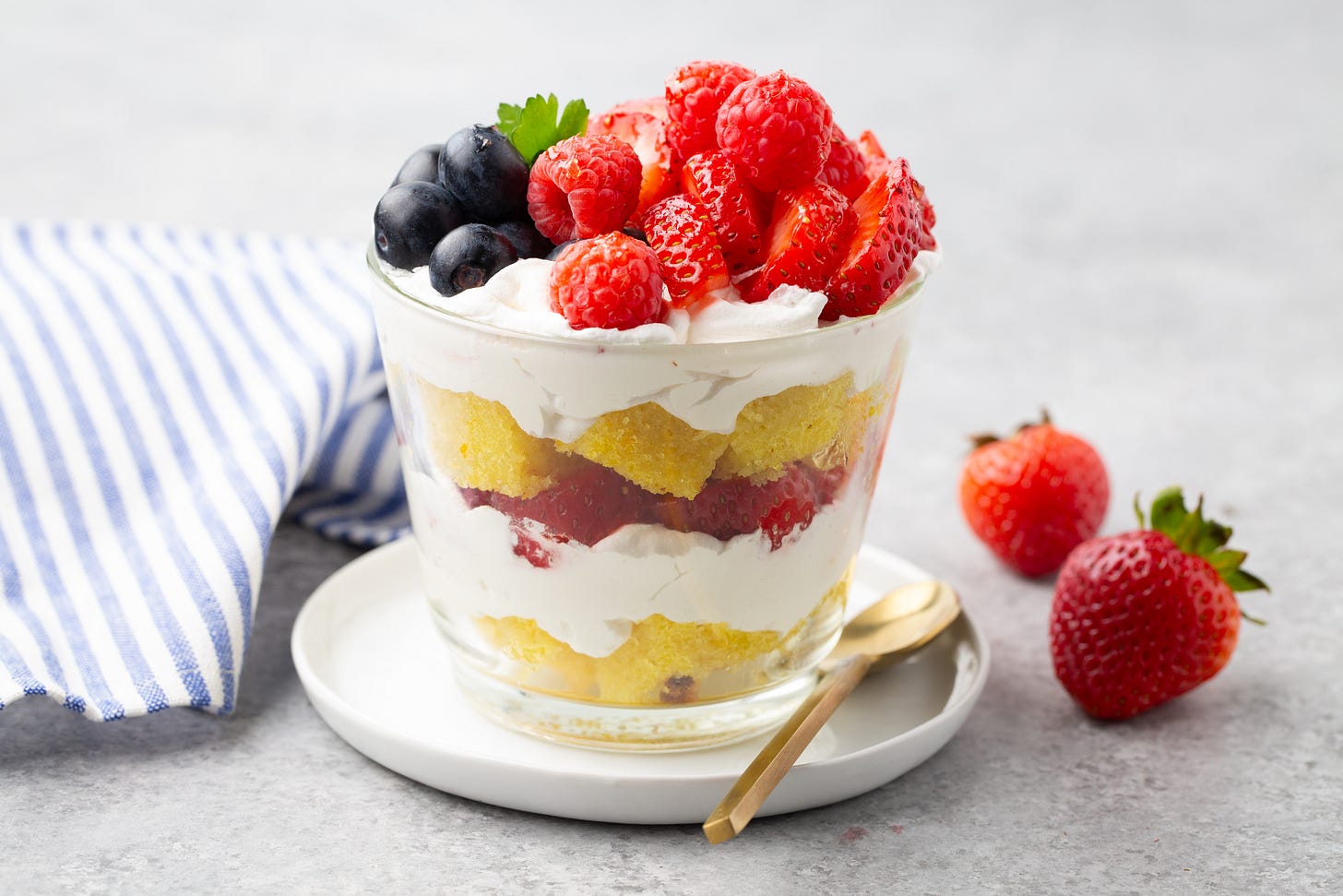 Summer Berry Trifles from Studio Delicious, the perfect warm weather dessert. Layers of cream and berries in a jar with a spoon. 