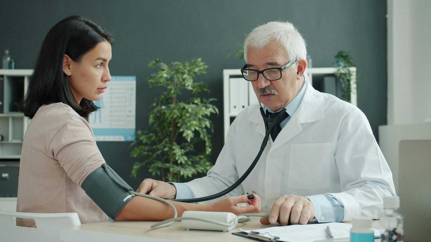 A doctor checking a patient’s blood pressure with an arm cuff and a stethoscope