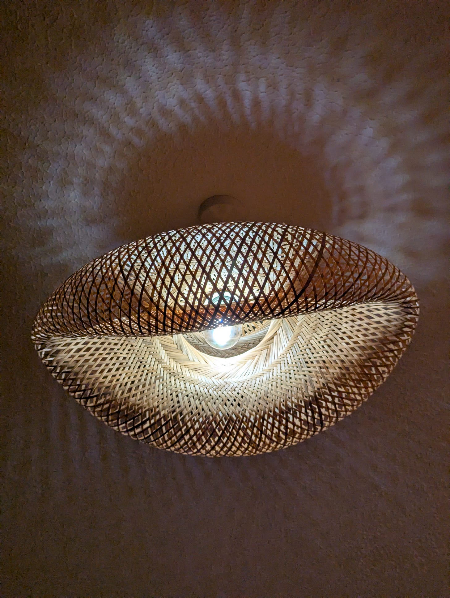 A light fixture made of weaved bamboo, hanging from a lit lightbulb.