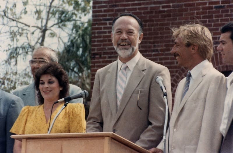 three people stand behind a lectern with microphones three people stand behind a lectern with microphones