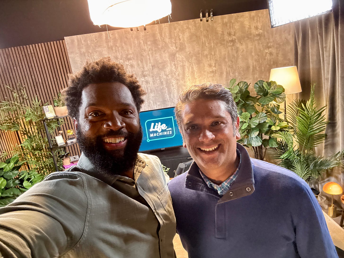 Baratunde Thurston takes a joyful selfie with Raj De Datta on the set of Life With Machines, both grinning wide under studio lights. Behind them, the show’s logo glows on a screen nestled among a jungle of houseplants, warm lamps, and cozy textures. It’s giving “tech talk meets living room vibes”—a perfect setting for a smart, soulful conversation. Baratunde Thurston takes a joyful selfie with Raj De Datta on the set of Life With Machines, both grinning wide under studio lights. Behind them, the show’s logo glows on a screen nestled among a jungle of houseplants, warm lamps, and cozy textures. It’s giving “tech talk meets living room vibes”—a perfect setting for a smart, soulful conversation.