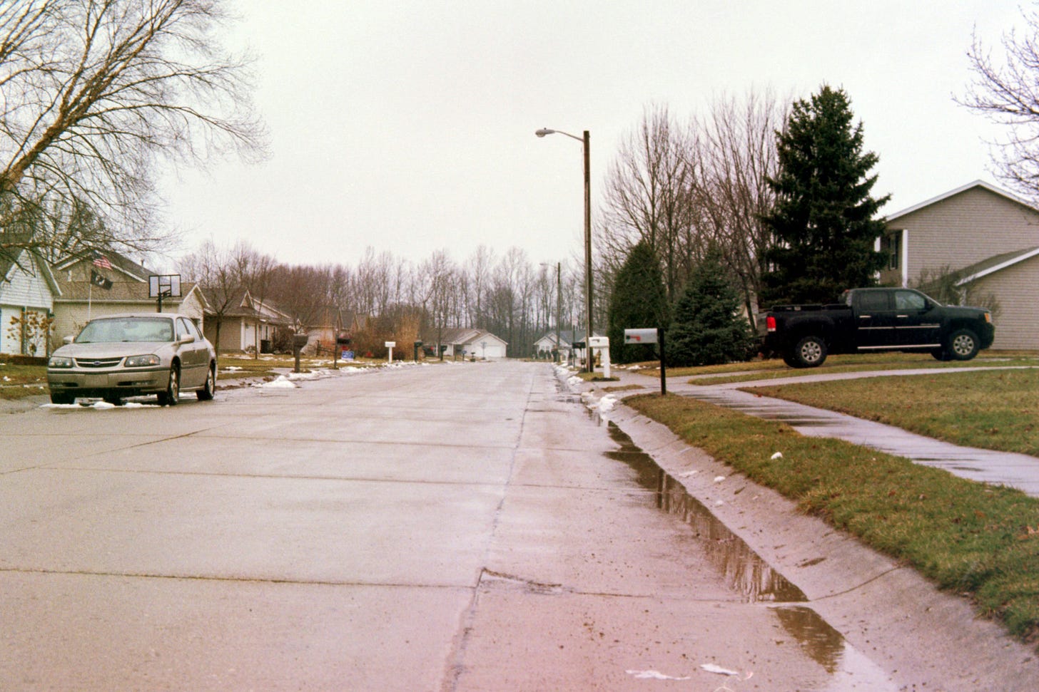 Empty neighborhood street with trash in the gutter and two abandoned cars
