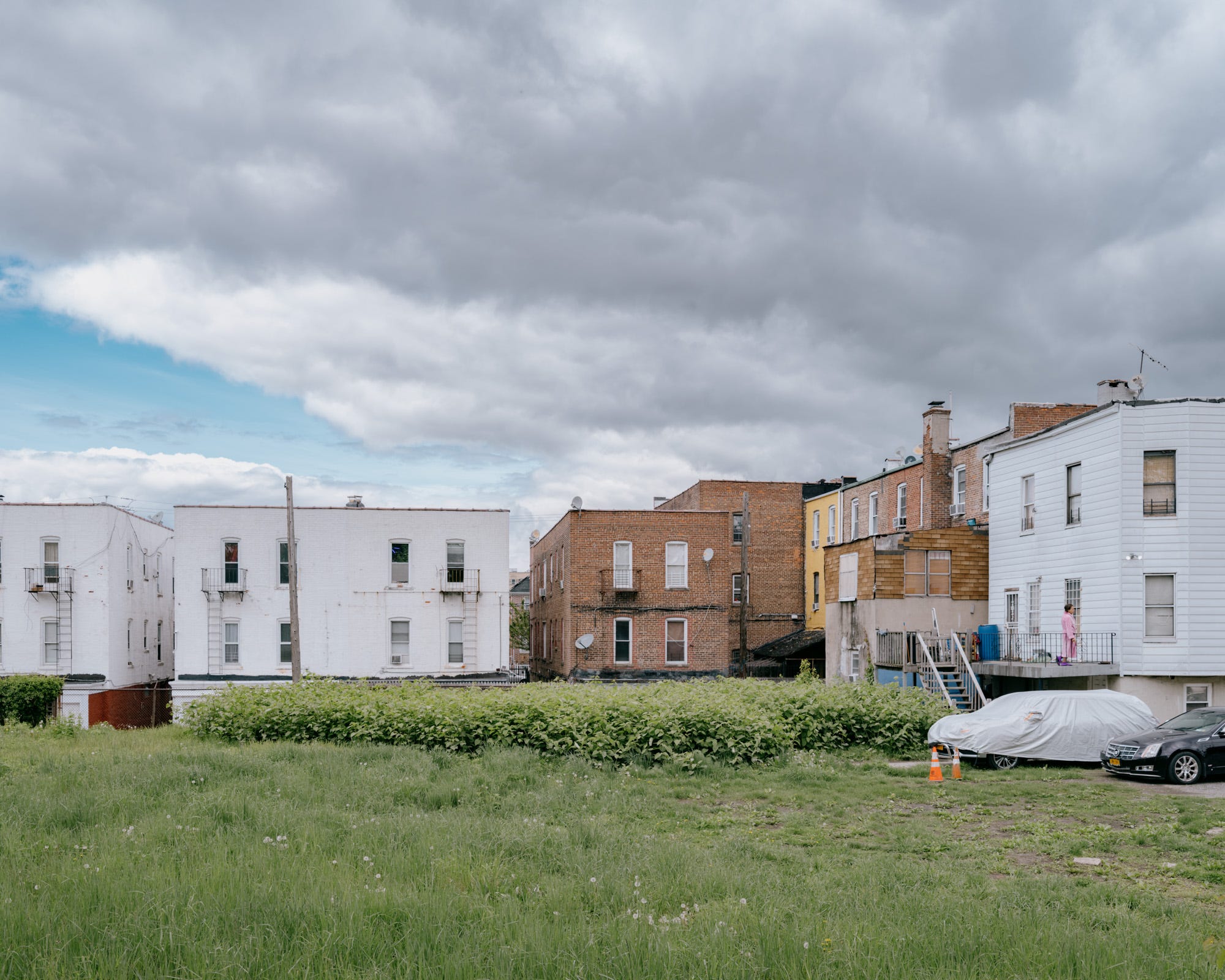 behind-row-of-houses-withgrass-and-woman-in-pink-bathroom-on-porch-