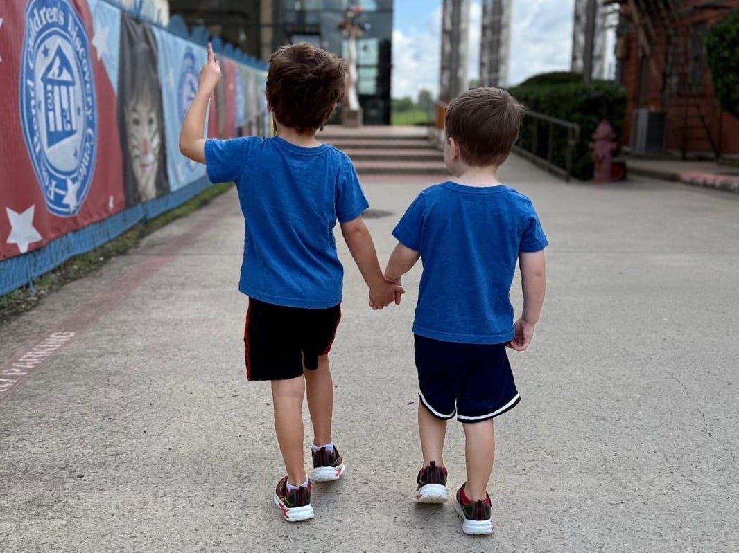 a five year old and a three year old boy wearing blue shirts and black shorts walking holding hands a five year old and a three year old boy wearing blue shirts and black shorts walking holding hands