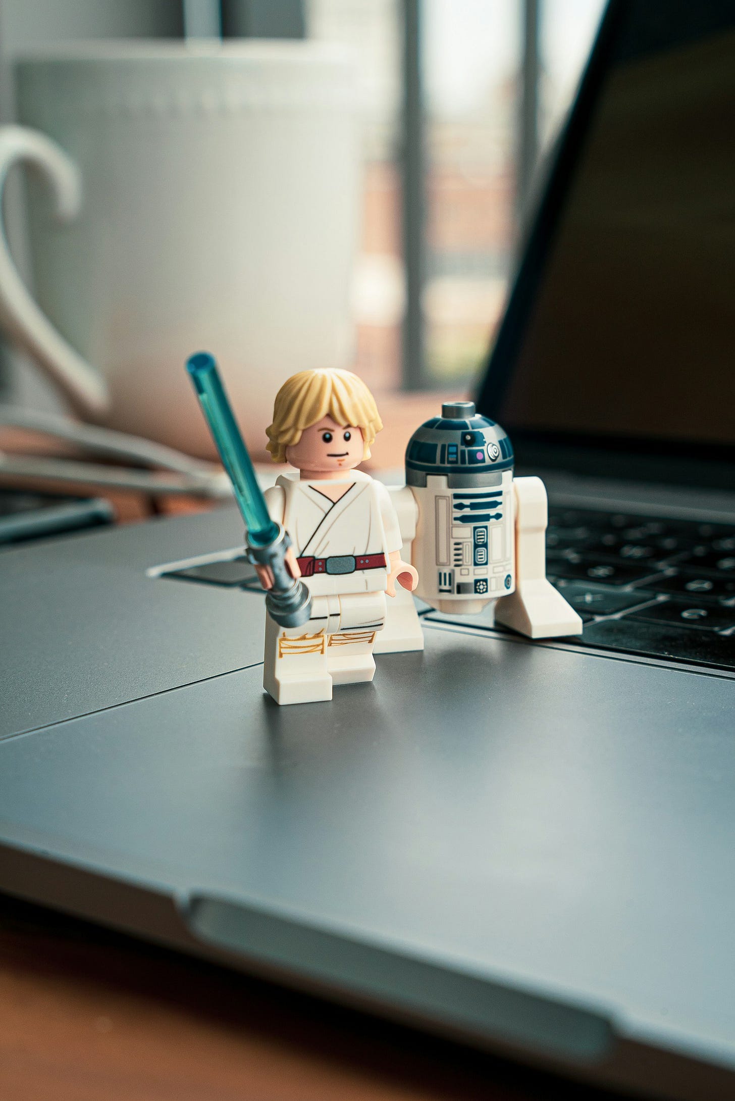 A Lego figure of Luke Skywalker holding a lightsaber, standing next to Lego R2D2; both on the surface of an open laptop.