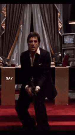 a man in a suit is sitting on a red carpet and holding a gun with the words say hello to my little friend above him a man in a suit is sitting on a red carpet and holding a gun with the words say hello to my little friend above him