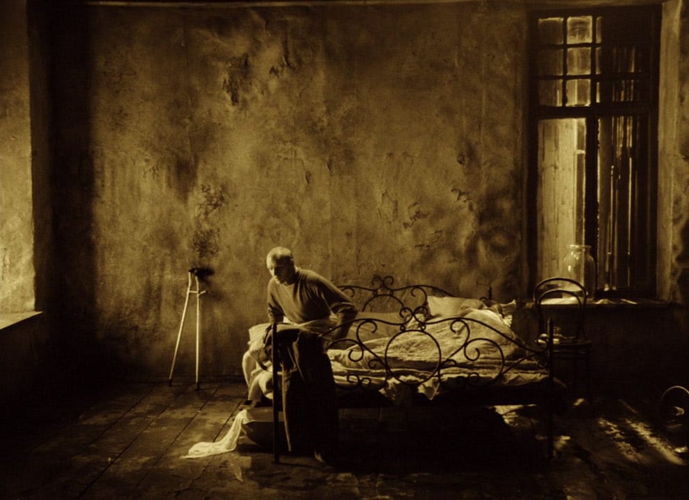 Scene in Stalker's apartment; he sits on a bed in a dilapidated room; the whole shot is tinted brown
