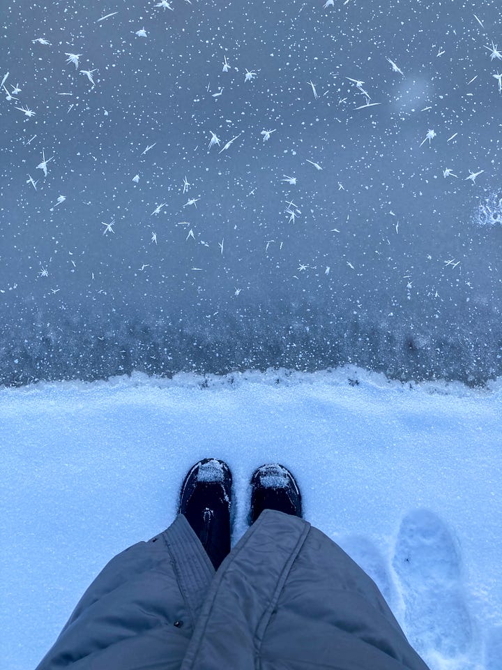 a person stands in the snow at the edge of a frozen lake, a person takes a photo out of a car window showing the wing mirror and the sun setting over a field