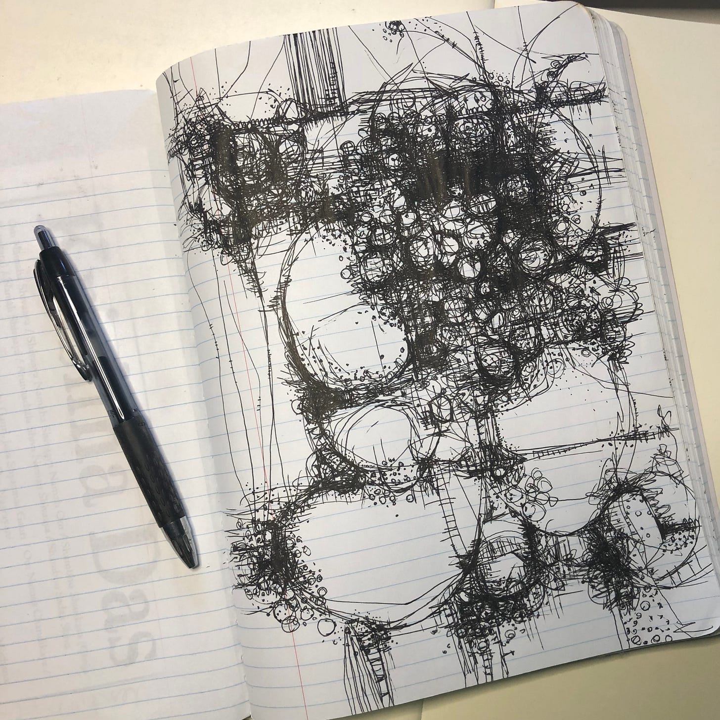 a photo of a notebook with a full page of scribbled lines and circles. A black pen lies on the left side of the open notebook.