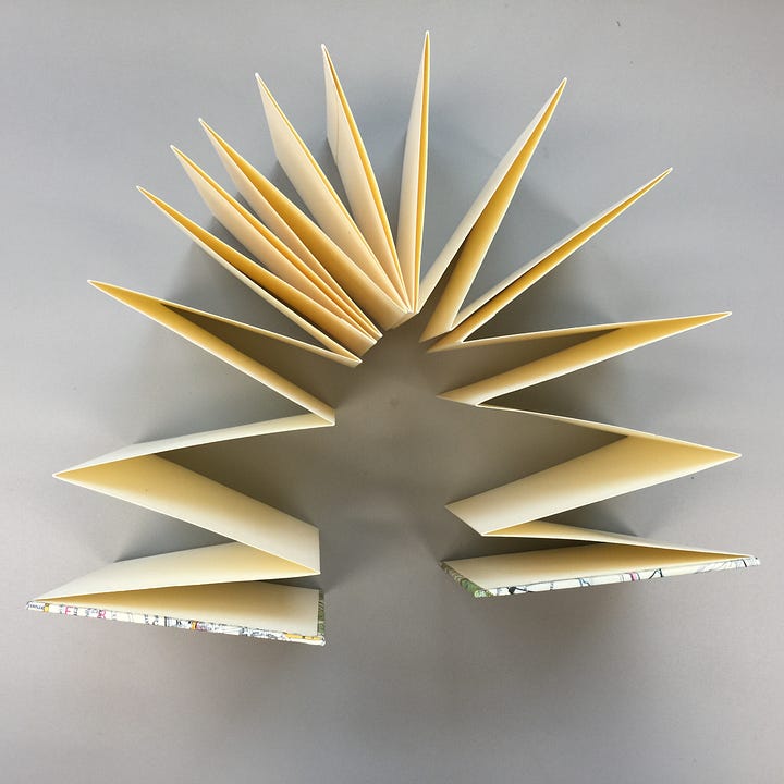 An accordion binding, first image: back and front hard cover, wrapped in map paper, a peak of cream paper folded in between. second image: an overhead view of the folded pages shaped like a U.