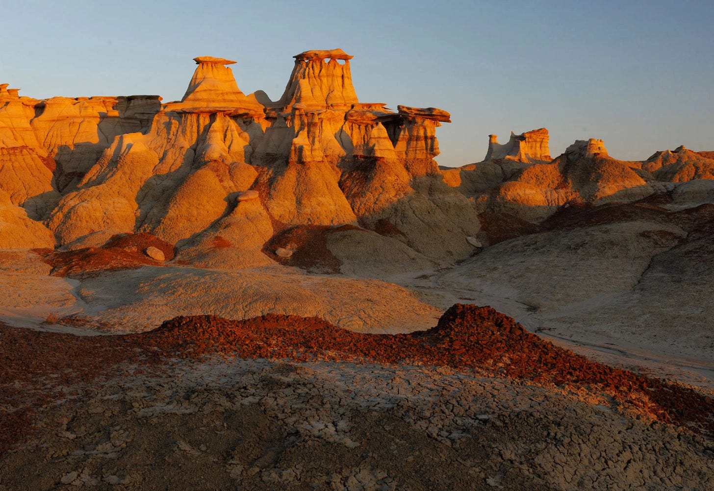 Sunset illuminates tall, layered hoodoos and orange-toned hills in the Bisti/De-Na-Zin Wilderness of New Mexico.