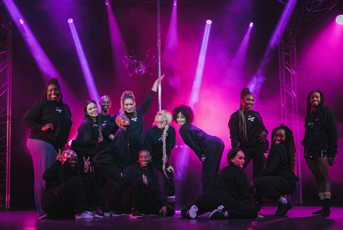 Group of Blackstage Pole performers standing under purple neon lights