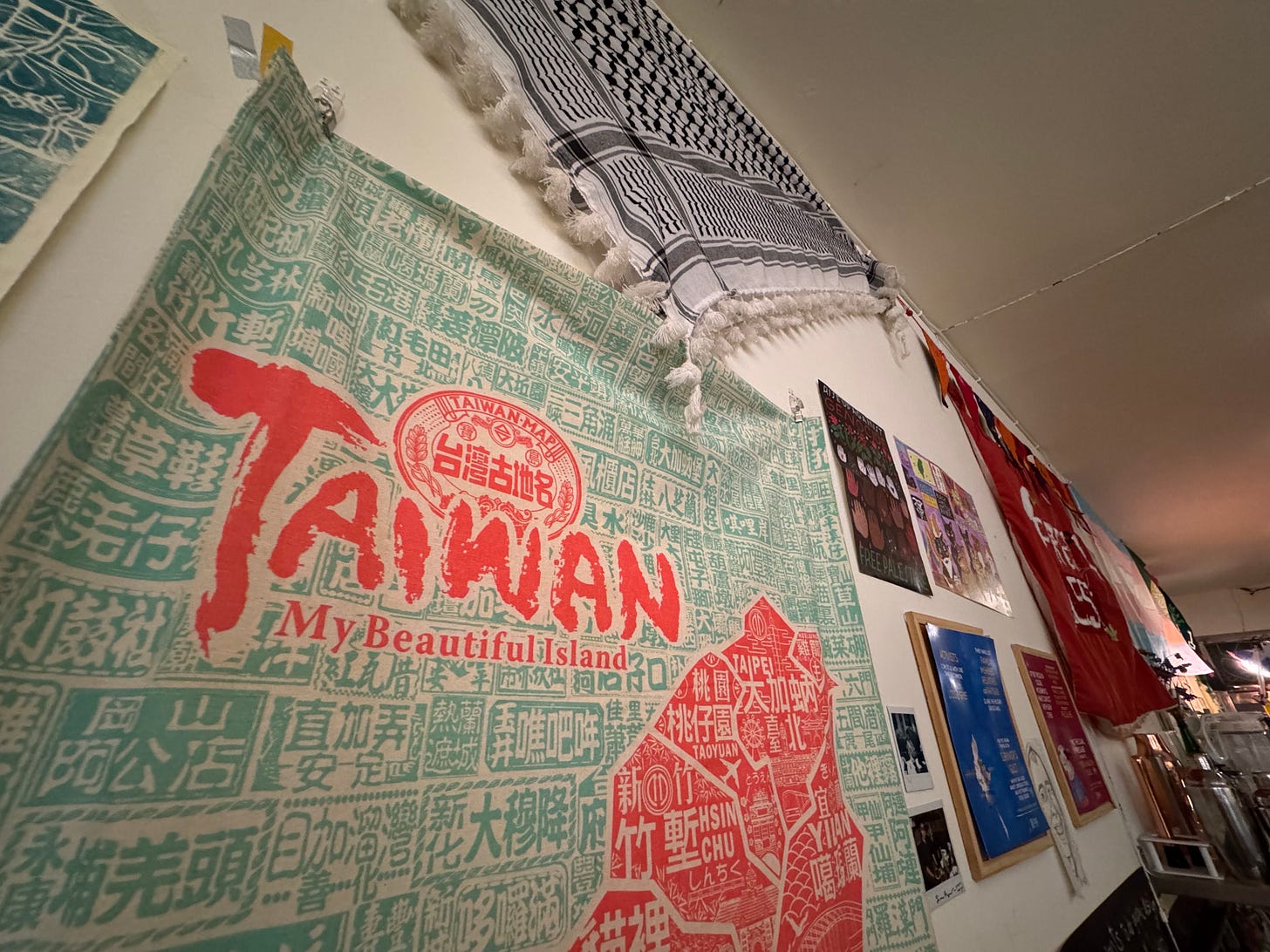 Horizontal 0.5 photo of a cloth hanging with the words Taiwan My Beautiful Island, underneath a keffiyeh, and other decor hanging on the walls of Daybreak.