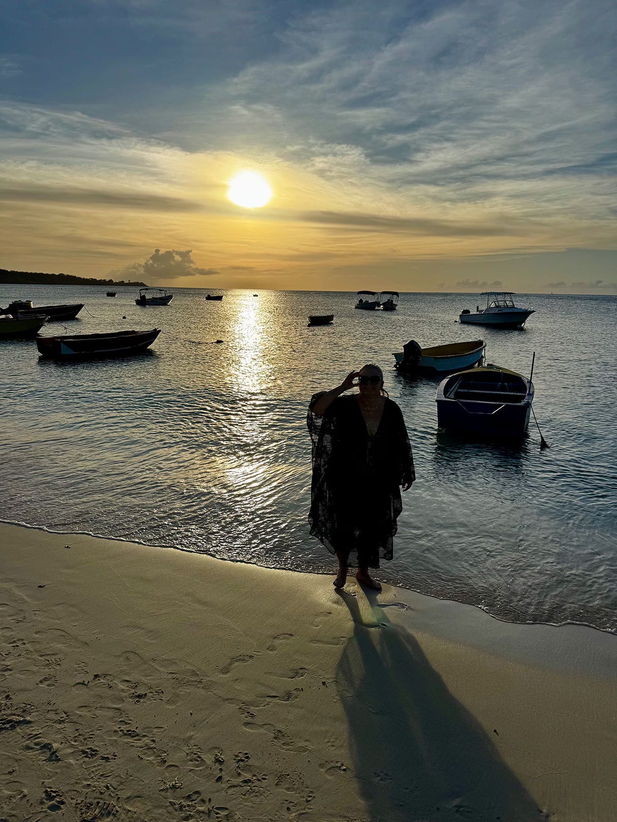 Woman standing in shallow ocean water at sunset in Grenada with boats and golden light on the water