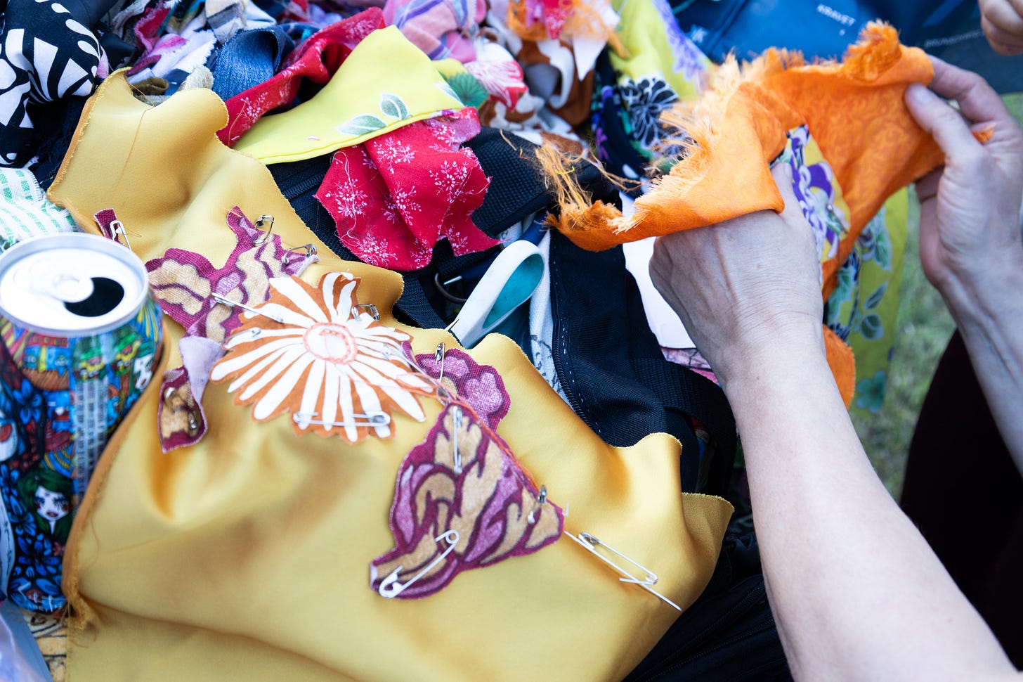 Multi-colored pile of scraps of fabric with a hand holding a scrap of bright orange, getting ready to mend.