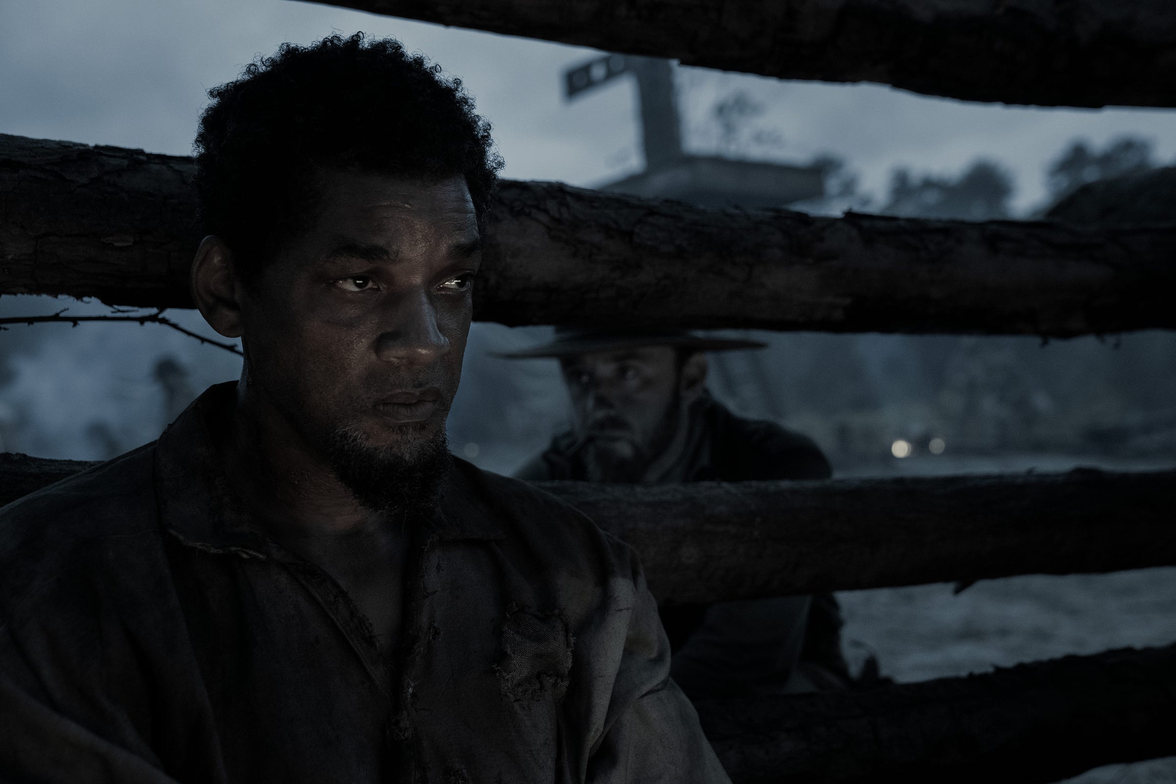 In character and in the background, actor Ben Foster stares at the back of Will Smith's head, who is looking ahead.