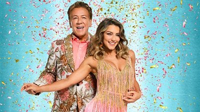 Ross wears a light floral patterned suit and peach shirt while Jowita wears a peachy pink and gold fringe trimmed dress