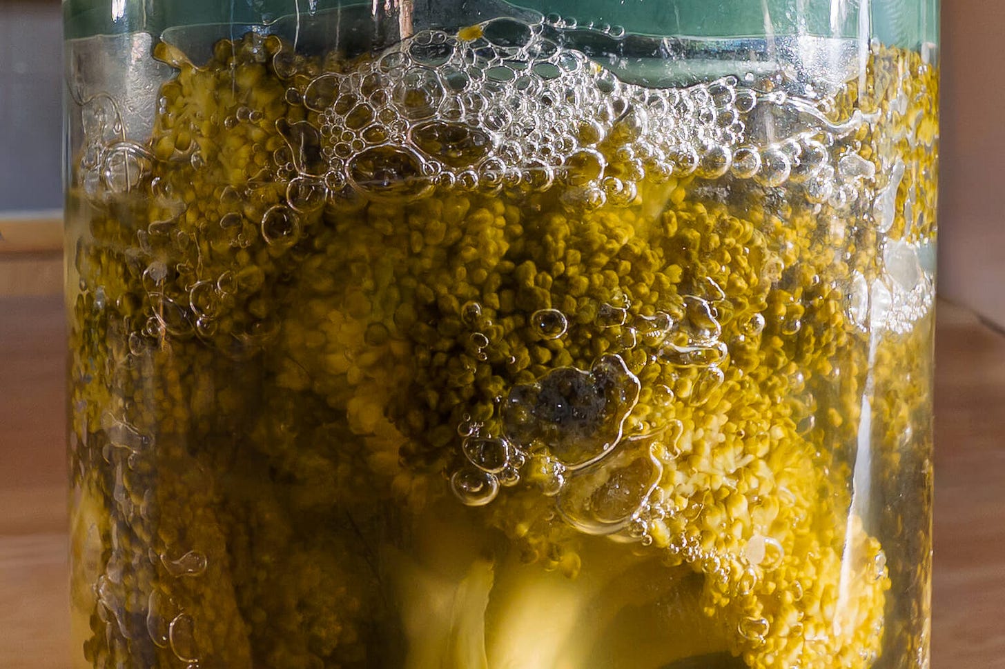 Close-up of broccoli florets in a jar of fermentation brine, surrounded by many small and large bubbles — a clear sign of active fermentation. Close-up of broccoli florets in a jar of fermentation brine, surrounded by many small and large bubbles — a clear sign of active fermentation.