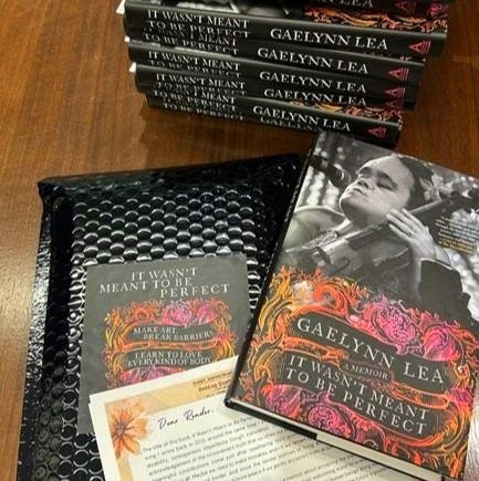 There is a stack of Gaelynn Lea's books on a desk, and in front of the pile there is one copy of her book and a letter to the readers, next to a mailing envelope. Gaelynn's publishing team sent her this photo when they were packing up the early reader copies There is a stack of Gaelynn Lea's books on a desk, and in front of the pile there is one copy of her book and a letter to the readers, next to a mailing envelope. Gaelynn's publishing team sent her this photo when they were packing up the early reader copies