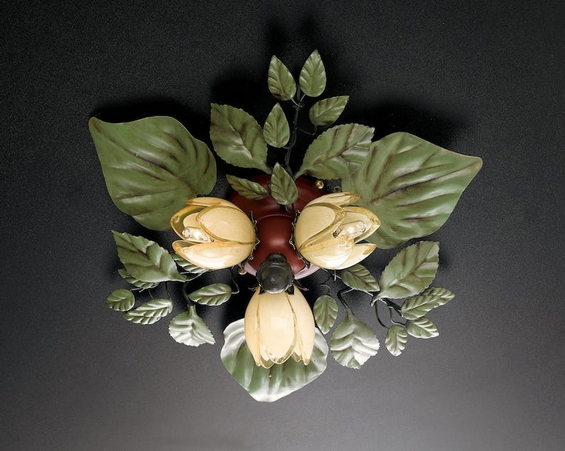 May include: A ceiling light fixture with three light bulbs shaped like flowers. The flowers are white with a yellow center and are surrounded by green metal leaves.