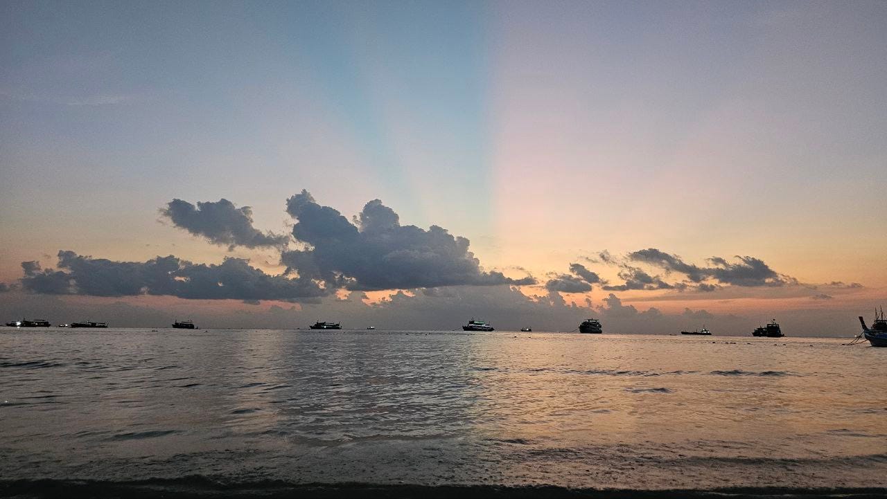 image of a sunset by the beach with boats on the horizon