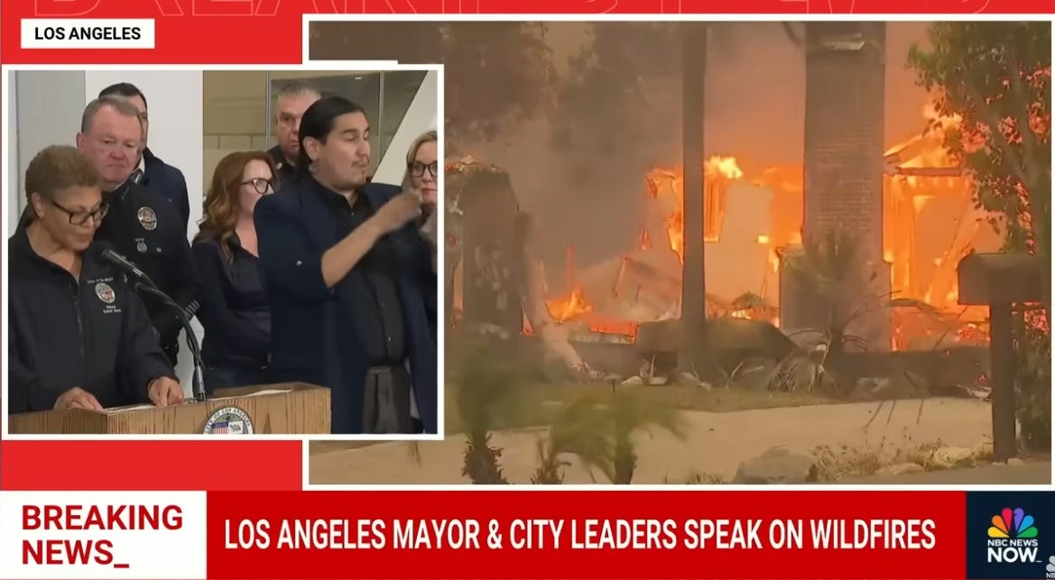Screenshot of NBC News split-screen coverage. In an inset view, LA Mayor Karen Bass, with other city officials behind her, speaks live at a press conference. In the larger video frame, B-roll of burning buildings and hillsides is on a loop. Chyron reads 'Breaking News: Los Angeles Mayor & City Leaders Speak ON Wildfires' Screenshot of NBC News split-screen coverage. In an inset view, LA Mayor Karen Bass, with other city officials behind her, speaks live at a press conference. In the larger video frame, B-roll of burning buildings and hillsides is on a loop. Chyron reads 'Breaking News: Los Angeles Mayor & City Leaders Speak ON Wildfires'