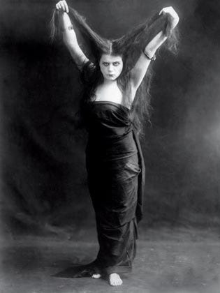 Publicity photo for the 1915 film Kreutzer Sonata features Theda Bara holding her arms up with a fistful of her long dark hair in each hand. She wears a low-cut black dress that exposes her arms and shoulders, and gazes defiantly into the camera. Publicity photo for the 1915 film Kreutzer Sonata features Theda Bara holding her arms up with a fistful of her long dark hair in each hand. She wears a low-cut black dress that exposes her arms and shoulders, and gazes defiantly into the camera.