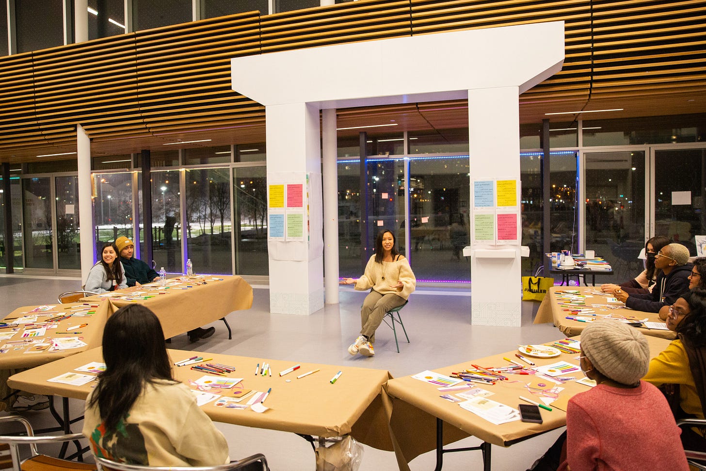 Tables arranged in a half circle with people seated around. Justine is sitting in the middle talking to the group.