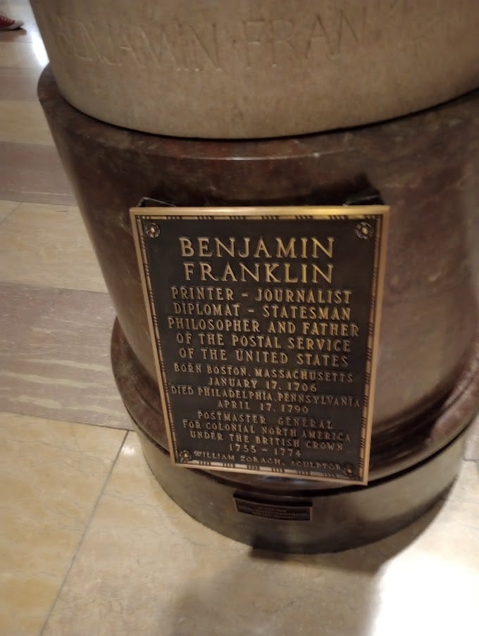 Left, statue of man in robes. Right, plaque explaining Franklin's accomplishments