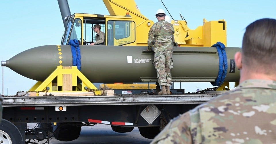 Military personnel loading a large bomb onto a flatbed truck.