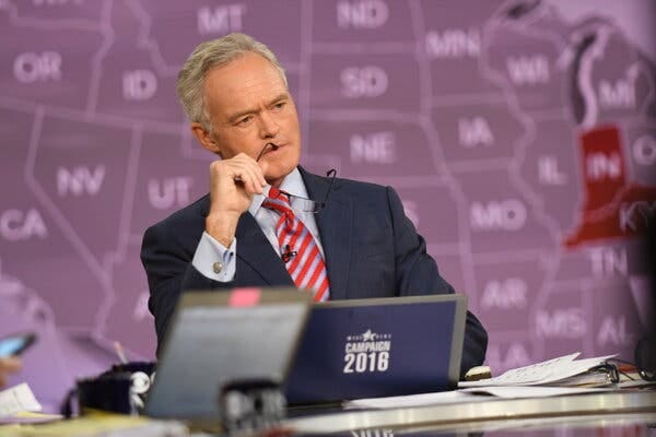 Scott Pelley sits in front of a map of the United States, holding his glasses to his lips.