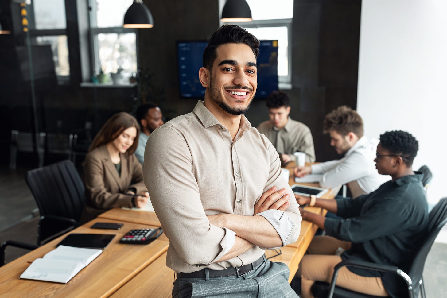 Successful professional stands in front of meeting table where his colleagues are gathering for a meeting Successful professional stands in front of meeting table where his colleagues are gathering for a meeting