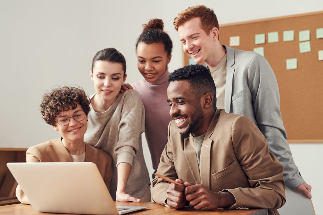 Free A group of diverse young professionals happily collaborating around a laptop indoors. Stock Photo