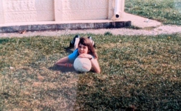 11-year-old me lying on the grass with a ball under my chin, posing for a photo