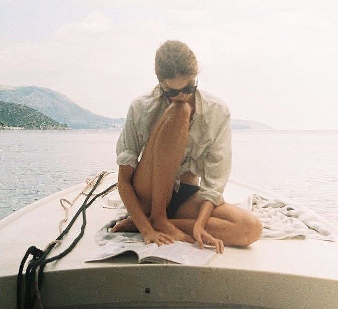 This may contain: a woman is sitting on the back of a boat reading a book while wearing sunglasses