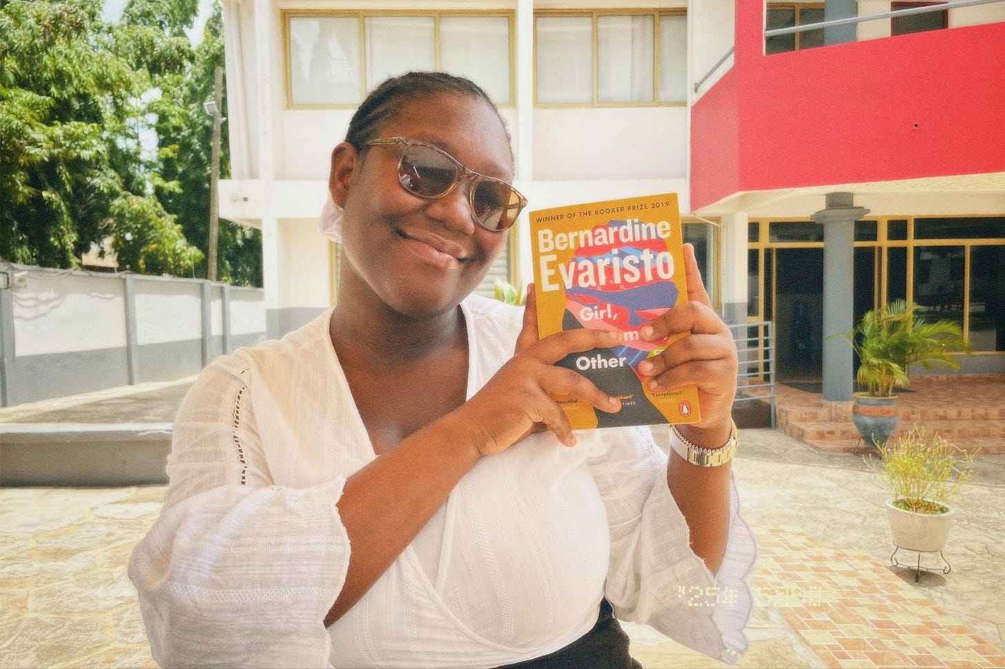 A woman with sunglasses smiling and holding up a book