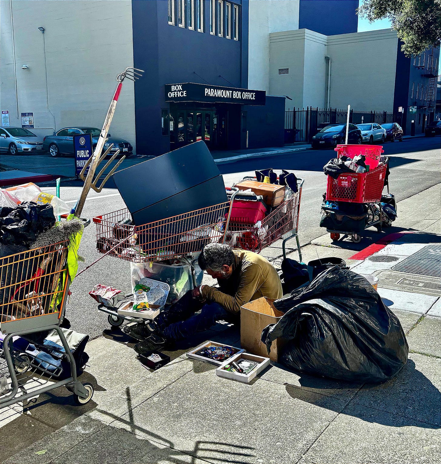A man rests on the curb on Thomas L. Berkeley Way in Oakland on Mar. 16, 2026. (Image source: Oakland Report)